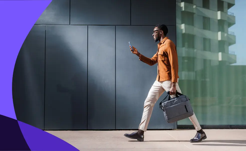A man in glasses walks confidently, holding a phone and a briefcase, against a modern building's backdrop.