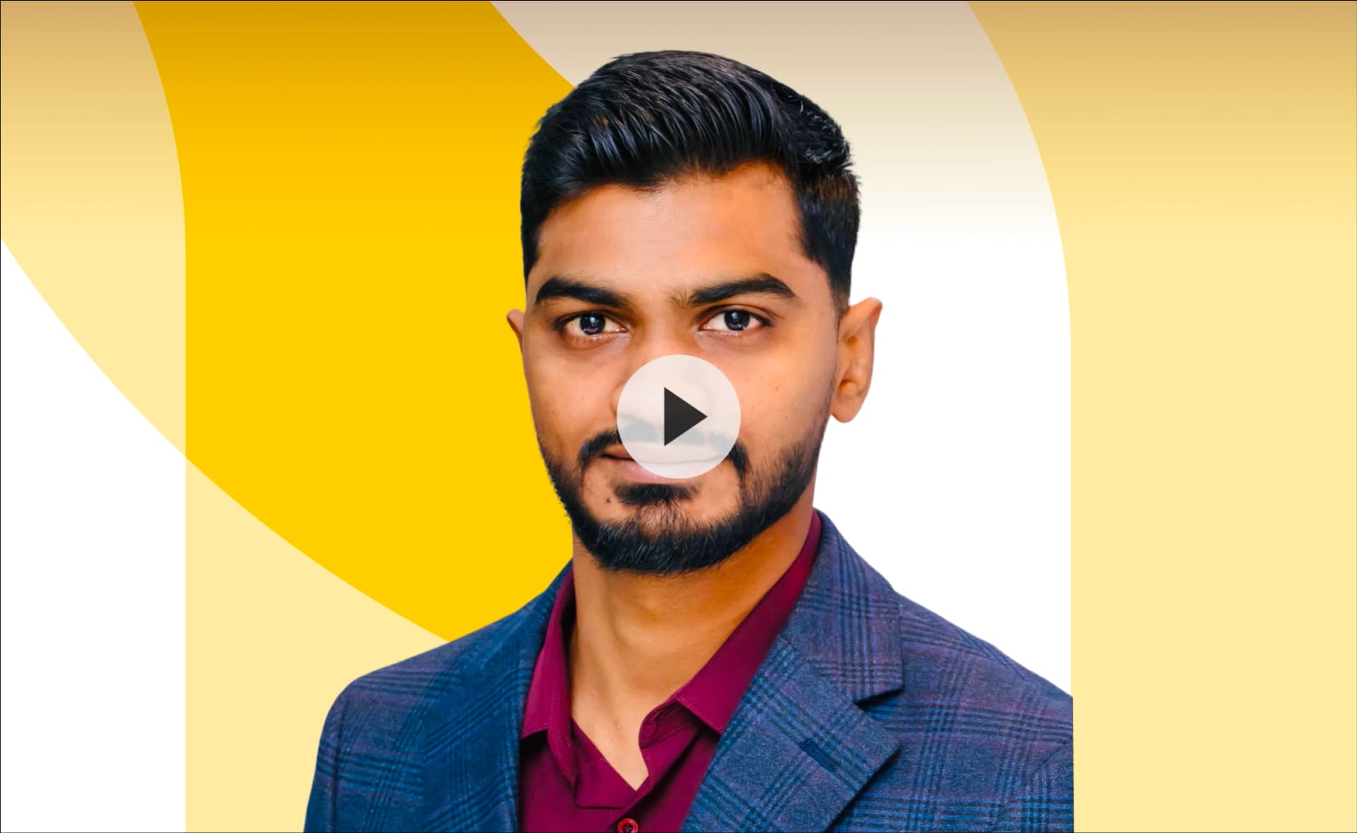 A man with short dark hair and a beard, wearing a plaid suit jacket and maroon shirt, is in front of a yellow and white abstract background.